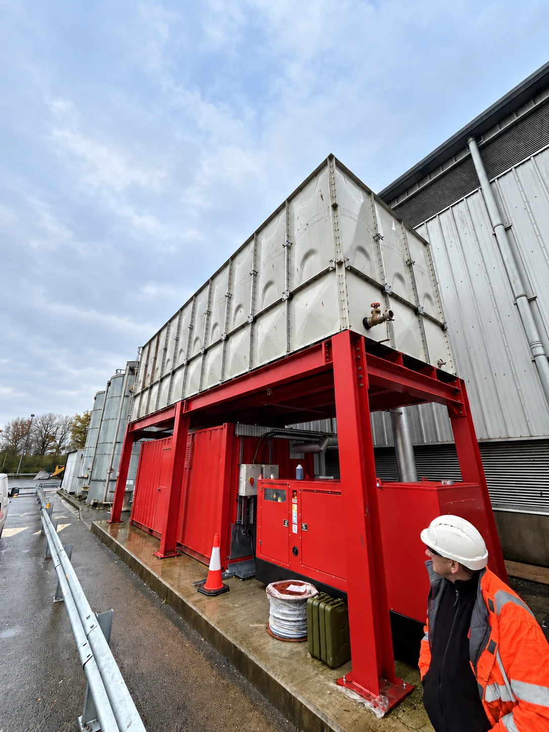 Elevated sectional water tank on red structural steelwork beside an industrial building