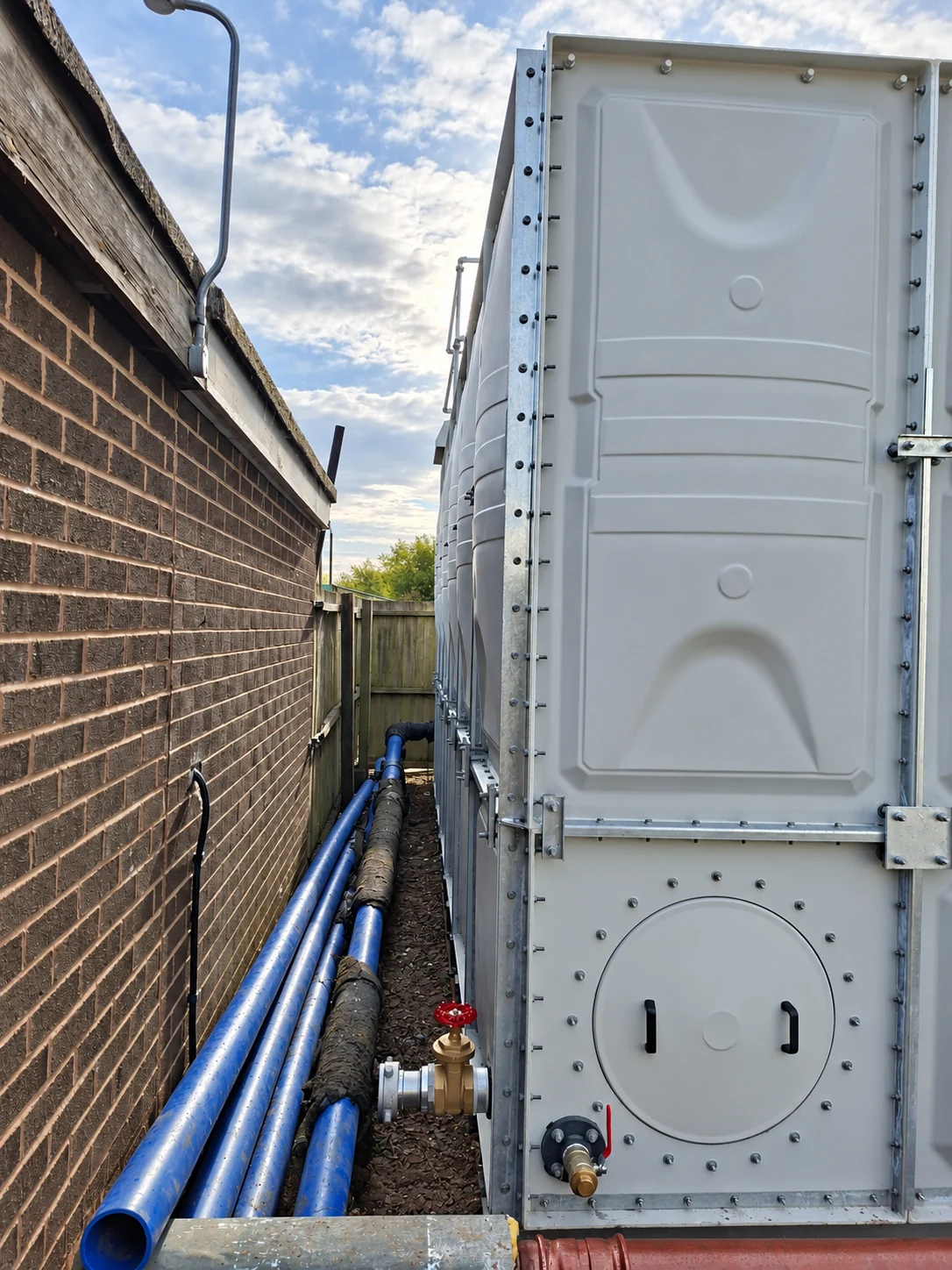 Sectional tank access panel and service connections beside an existing building