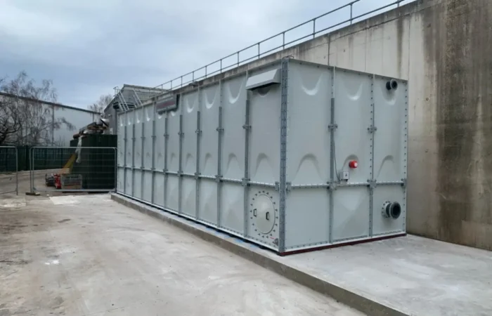 Large sectional GRP tank installed outdoors next to a concrete wall and site equipment