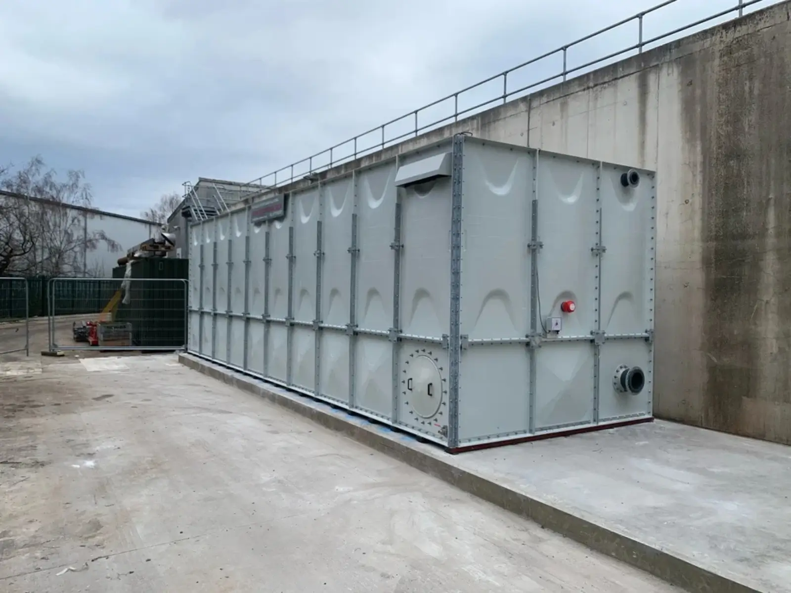 Large sectional GRP tank installed outdoors next to a concrete wall and site equipment